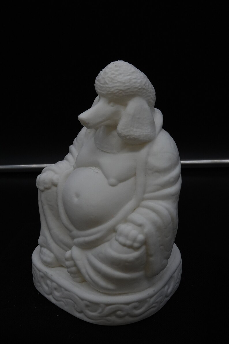 May include: A white sculpture of a seated Buddha with the head of a poodle. The figure is in a relaxed pose, with a large belly and draped robes. The base has a decorative, swirling pattern. The background is black.