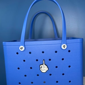 Op de afbeelding: Een blauwe tote bag met een witte skelethand die de middelvinger opsteekt. De tas heeft een wit "boga" logo aan de onderkant en witte letterknoppen aan de zijkanten.