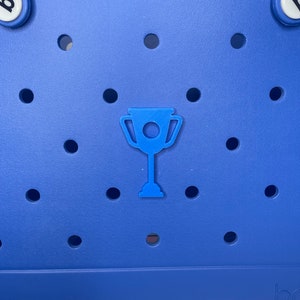 May include: A blue tote bag with a trophy charm. The bag has a  perforated design and a white handle.