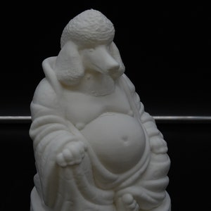 May include: A white sculpture of a seated Buddha with the head of a poodle. The figure is in a relaxed pose, with a large belly and flowing robes. The base has a decorative, carved design. The sculpture is set against a black background.