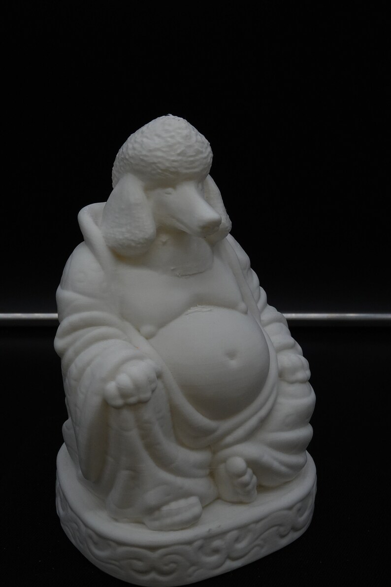 May include: A white sculpture of a seated Buddha with the head of a poodle. The figure is in a relaxed pose, with a large belly and flowing robes. The base has a decorative, carved design. The sculpture is set against a black background.