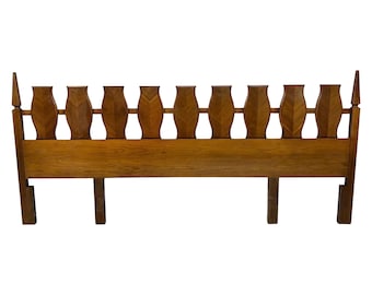 May include: A wooden headboard with a warm brown finish. The headboard features a series of decorative, vase-like cutouts across the top, with a solid base and legs. The design is mid-century modern.