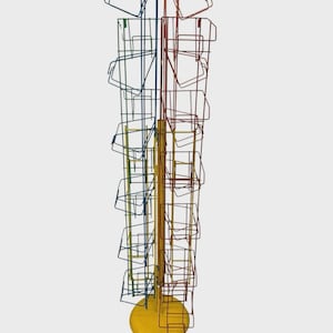 May include: A tall, multi-colored wire display rack with a yellow base. The rack features numerous rectangular compartments in shades of blue, red, green, and yellow, arranged vertically. The central pole is yellow.