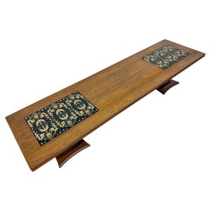 May include: A long, rectangular, wooden coffee table with two black and gold tiled inlays. The table has a dark wood finish and sits on four legs.