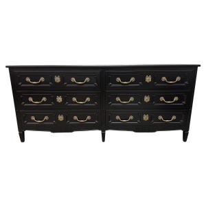 May include: A black dresser with six drawers, featuring brass-colored handles and keyhole details. The dresser has a rectangular shape with a slightly curved front and sits on short, tapered legs. The overall design is classic and elegant.