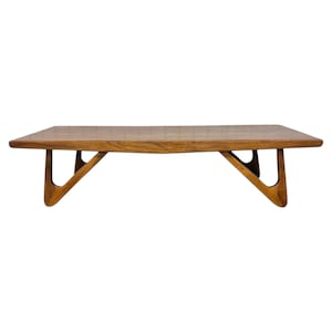 May include: A rectangular wooden coffee table featuring a smooth, polished brown surface with visible wood grain. The table is supported by four distinct, angular, V-shaped legs that extend outward from the center toward the corners.