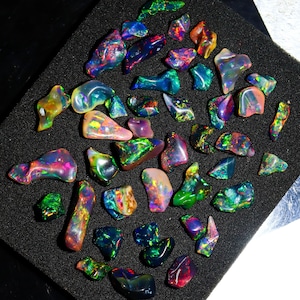 Peut inclure: Une collection de pierres précieuses d'opale irisées de différentes formes et tailles. Les opales sont un mélange de vert, bleu, rouge et violet.