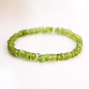 May include: A bracelet made of small, irregular-shaped, light green peridot gemstones. The gemstones are strung together, creating a circular form. The translucent gemstones give the bracelet a delicate appearance. The design is simple and elegant.