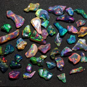 May include: A collection of polished opal gemstones in various shapes and sizes. The opals display a vibrant play of color, including shades of green, blue, purple, orange, and yellow. The gemstones are arranged on a black surface, showcasing their iridescent qualities.