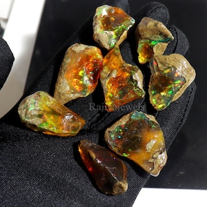 Op de afbeelding: Een verzameling ruwe opaal edelstenen. De opalen vertonen levendige kleuren, waaronder oranje, geel en groen, met flitsen van iriserendheid. De stenen hebben een natuurlijk, aards uiterlijk, met een ruwe, getextureerde buitenkant.