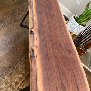 May include: A dark brown live edge wood coffee table with black metal legs. The table top has a natural wood grain pattern.