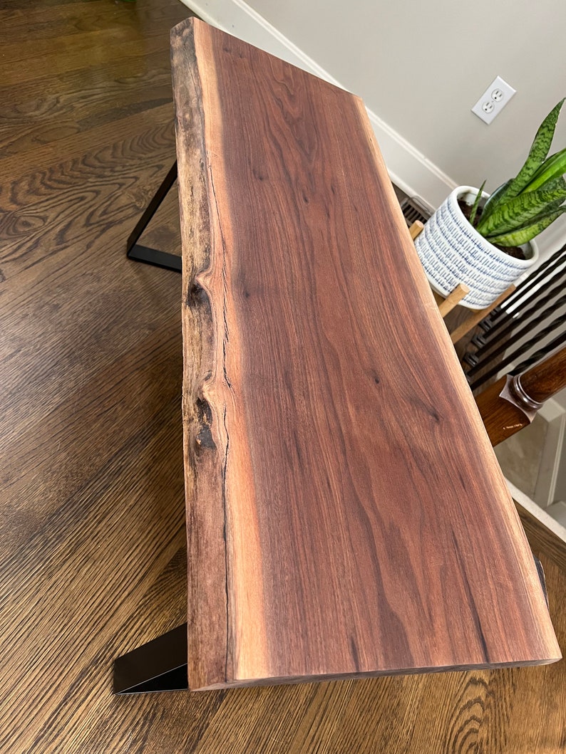 May include: A dark brown live edge wood coffee table with black metal legs. The table top has a natural wood grain pattern.