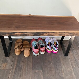 May include: A wooden bench with black metal legs. There are four pairs of shoes underneath the bench, including sandals and sneakers.