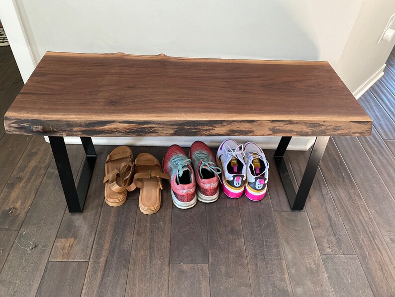 May include: A wooden bench with black metal legs. There are four pairs of shoes underneath the bench, including sandals and sneakers.