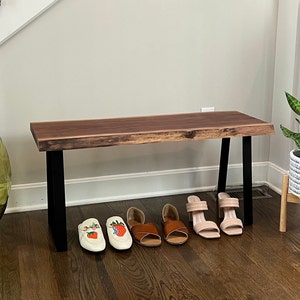 May include: A wooden bench with a live edge top and black metal legs. The bench is in a hallway and has shoes and a plant on the floor in front of it.