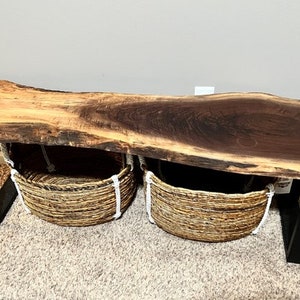 May include: A live edge walnut wood coffee table with black metal legs and two woven baskets underneath.