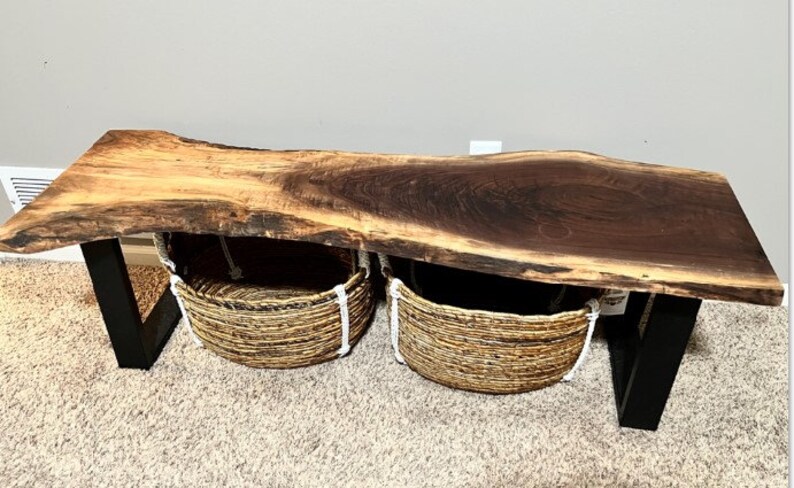 May include: A live edge walnut wood coffee table with black metal legs and two woven baskets underneath.