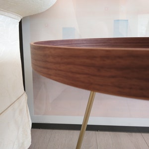 K&ouml;nnte beinhalten: Ein runder Holztisch mit einer dunkelbraunen Holzplatte und goldenen Metallbeinen. Der Tisch steht auf einem hellen Holzboden.