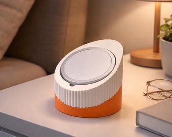 Op de afbeelding: Een moderne, tweekleurige draadloze oplader. De bovenkant is wit met een zilveren oplaadoppervlak en de basis is oranje. De oplader heeft een geribbelde textuur op het witte gedeelte en is schuin.