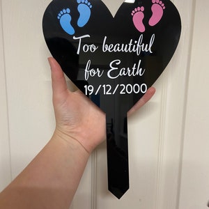 May include: Black heart-shaped memorial plaque with blue and pink footprints and the text "Too beautiful for Earth 19/12/2000".