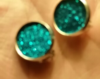 May include: A pair of round, teal blue earrings with a sparkly finish.