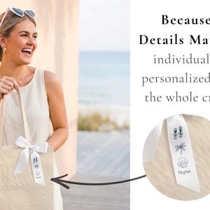 May include: A beige canvas tote bag featuring a white satin ribbon tied to the handle. The ribbon is printed with black line art icons of two champagne flutes, a palm tree, a seashell, and the name Peyton in a simple script font.
