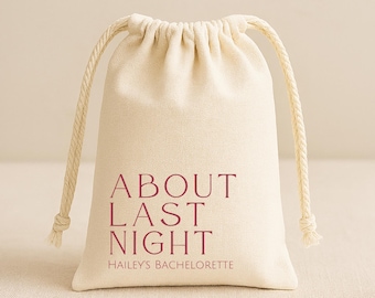 May include: A cream-colored fabric drawstring pouch featuring the maroon text ABOUT LAST NIGHT and HAILEY'S BACHELORETTE printed on the front. The bag has a gathered top with two thick, matching cream-colored twisted rope drawstrings on each side.