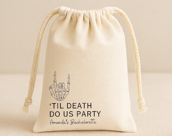 May include: A cream-colored fabric drawstring pouch featuring a black graphic of a skeleton hand making a rock-and-roll gesture. The text reads 'TIL DEATH DO US PARTY' in a bold sans-serif font, followed by 'Amanda's Bachelorette' in script.