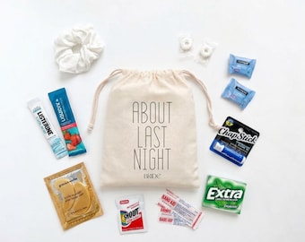 May include: A beige drawstring canvas bag with the text ABOUT LAST NIGHT BRIDE printed in black, surrounded by a white scrunchie, Listerine Cool Mint, Liquid IV, two mints, two blue packets, ChapStick, Extra gum, Shout wipe, and gold eye masks.