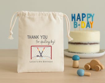May include: A cream-colored drawstring gift bag with the text "THANK YOU for skating by!" and a hockey-themed graphic. The bag is personalized with "LUCAS'S 4TH BIRTHDAY". A birthday cake and wooden toys are in the background.
