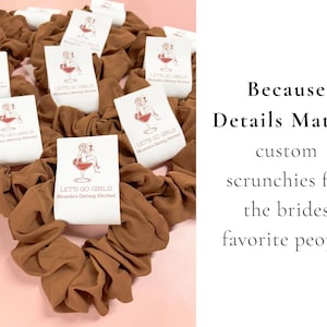 May include: A collection of brown fabric hair scrunchies, each featuring a white paper tag printed with a red graphic of a person in a wine glass and the text "LET'S GO GIRLS Miranda's Getting Hitched." The text "Because Details Matter" is visible.