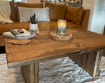 Könnte beinhalten: Ein rustikaler Holz-Couchtisch mit natürlicher Holzoptik. Der Tisch hat eine rechteckige Tischplatte und zwei rechteckige Beine. Der Tisch steht auf einem weißen, flauschigen Teppich. Eine Kerze steht auf einer Holzscheibe auf dem Tisch.