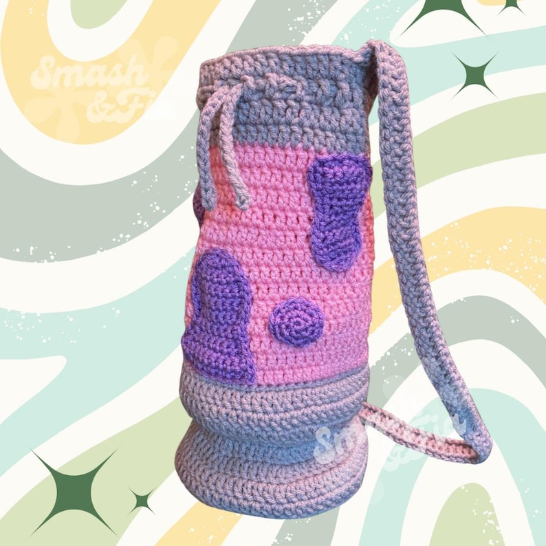 May include: A crocheted bag with a pink and purple spotted design and a grey strap. The bag has a drawstring closure.