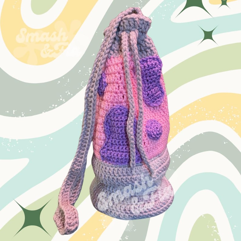 May include: A crocheted drawstring bag with a purple and pink spotted design. The bag has a long strap and is made with a grey yarn.