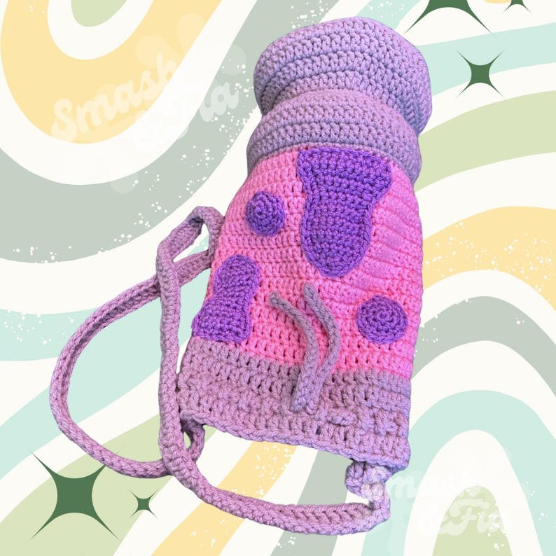 May include: A crocheted purple and pink bag with a strap. The bag has a cartoon-like design with purple spots and a purple face.