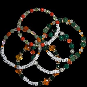 Pu&ograve; includere: Quattro braccialetti di perline su sfondo nero. I braccialetti presentano una variet&agrave; di perline colorate, tra cui rosse, verdi, arancioni e trasparenti. Alcuni braccialetti hanno perline con lettere bianche che compongono frasi come "ACTUALLY ROMANTIC" e "WISH OF OPHELIA".