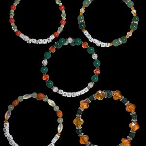 Pu&ograve; includere: Cinque braccialetti di perline con vari schemi di colori e testo. Un braccialetto dice "WISH LIST" con perline rosse e bianche. Un altro dice "OPALITE" con perline verdi. Il terzo dice "ACTUALLY ROMANTIC" con perline arancioni. Il quarto dice "HONEY" con perline arancioni.