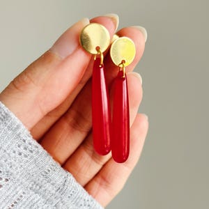 May include: A pair of red teardrop-shaped earrings with gold disc accents.