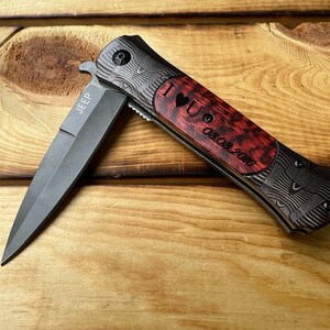Puede incluir: Un cuchillo de bolsillo negro y gris con un mango de madera rojo y negro. El mango est&aacute; grabado con "I love you 08.03.2016" y la hoja est&aacute; grabada con "JEEP".