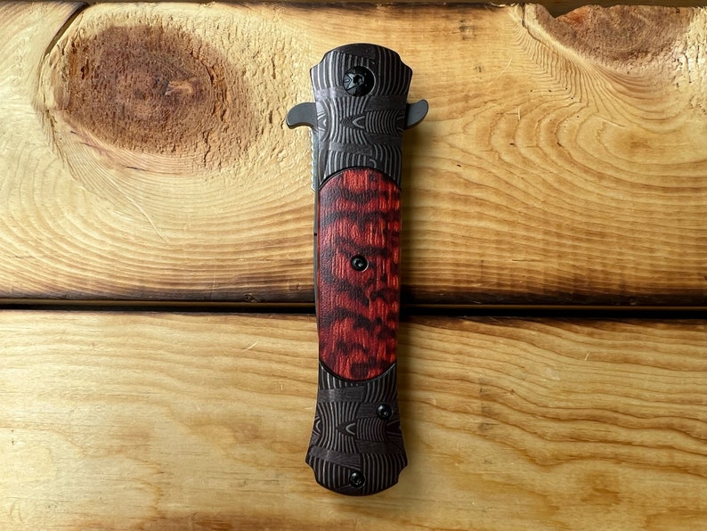 Puede incluir: Un cuchillo de bolsillo negro y rojo con un mango estampado. El mango est&aacute; hecho de madera y metal.