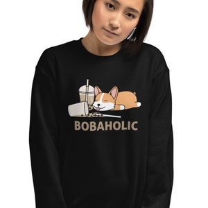 Może przedstawiać: Czarna bluza z nadrukiem kreskówkowego corgi śpiącego na rozlanym bubble tea. Pod nadrukiem znajduje się napis "BOBAHOLIC".