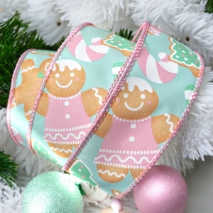 May include: A 2.5 inch wide ribbon with a light blue background and a pink gingerbread pattern. The ribbon features gingerbread people, candy canes, and Christmas trees.