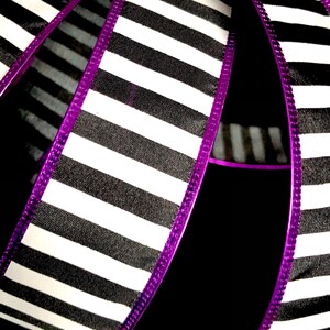 May include: Black and white striped ribbon with a purple edge. The ribbon is folded in half and the stripes are running vertically.