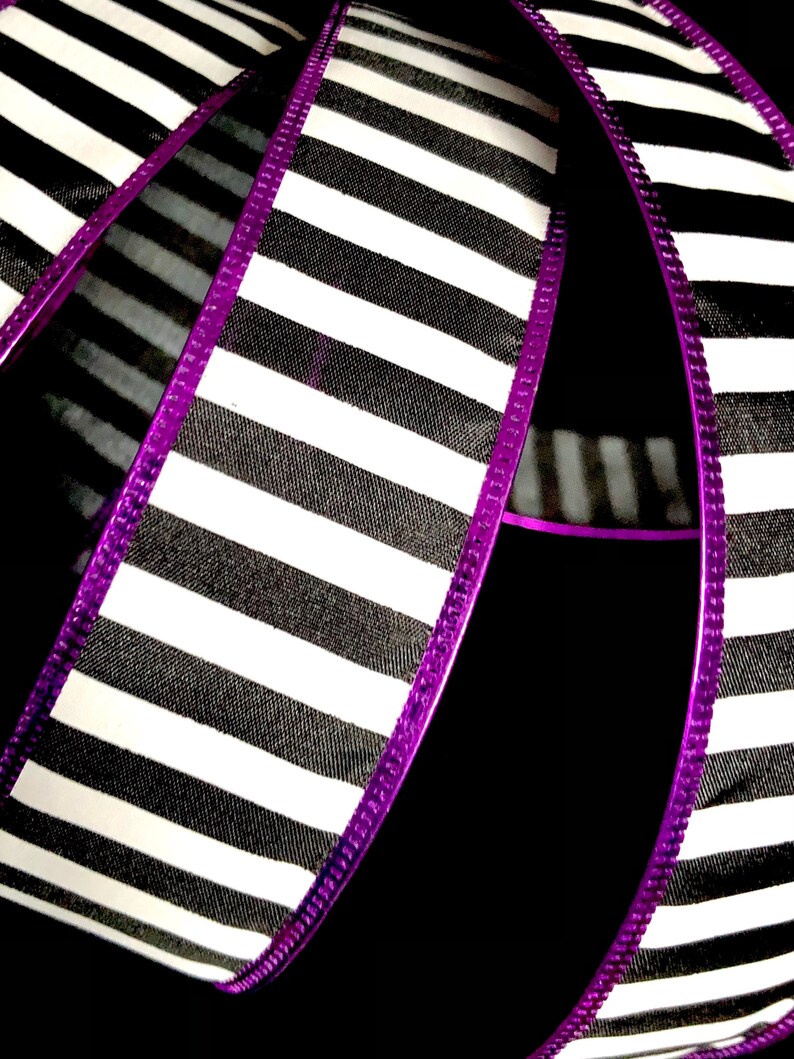 May include: Black and white striped ribbon with a purple edge. The ribbon is folded in half and the stripes are running vertically.