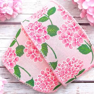 May include: Pink and green floral ribbon with a hydrangea design. The ribbon has a textured, linen-like surface and a scalloped edge.