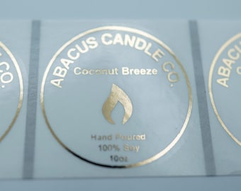 May include: Three gold foil stickers with a circular design. The stickers say "ABACUS CANDLE CO." and "Coconut Breeze". The stickers also say "Hand Poured 100% Soy 100ml".
