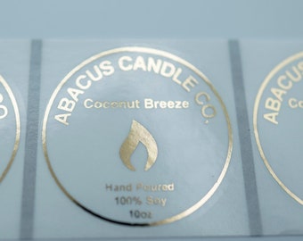 May include: Three gold foil stickers with a circular design. The stickers say "ABACUS CANDLE CO." and "Coconut Breeze". The stickers also say "Hand Poured 100% Soy 100ml".