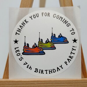 May include: Round white sticker with black text that says "Thank you for coming to Leo's 4th Birthday Party!" with three cartoon bumper cars in red, green, and blue.