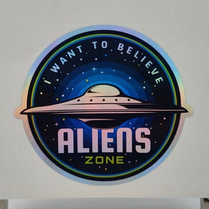 Może przedstawiać: Holograficzna naklejka w kolorze niebieskim, zielonym i fioletowym. Naklejka przedstawia latający spodek z tekstem "I want to believe" i "Aliens Zone".