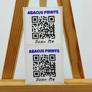 Puede incluir: Dos pegatinas cuadradas blancas con códigos QR en blanco y negro. Las pegatinas tienen el texto "ABACUS PRINTS" y "Scan Me" en azul.